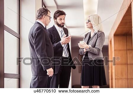 Stock Image - Businessmen and woman having discussions in office corridor. Fotosearch