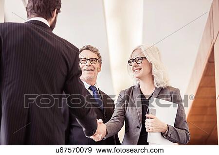 Stock Photo - Businessmen and woman shaking hands in office corridor. Fotosearch