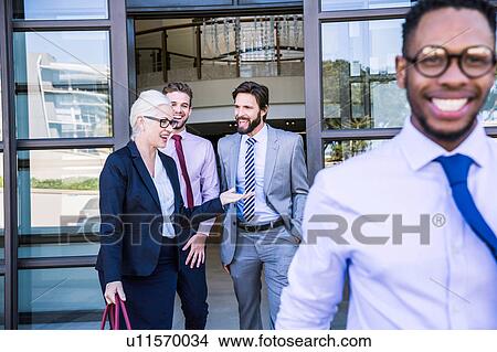 Picture - Businessmen and woman talking whilst leaving office building. Fotosearch