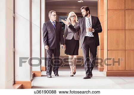 Businessmen and woman walking and talking in office corridor View Large Photo Image Stock Photo - Businessmen and woman walking and talking in office corridor. Fotosearch
