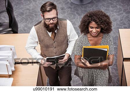 Stock Image - Businesswoman and man carrying files in office. Fotosearch