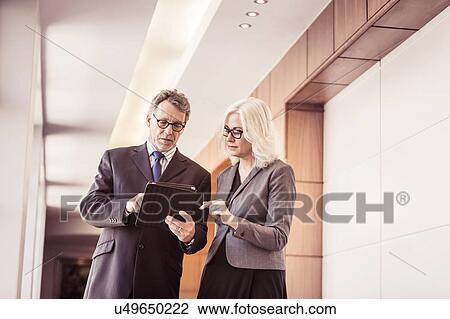 Stock Image - Businesswoman and man using digital tablet in office corridor. Fotosearch
