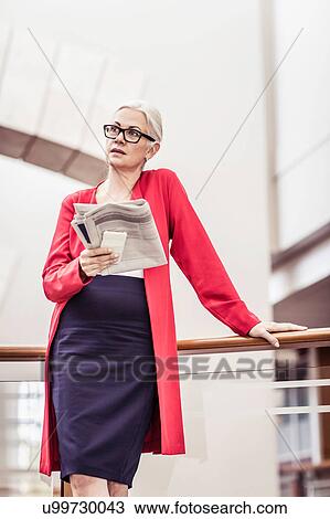 Stock Image - Businesswoman reading newspaper on office balcony. Fotosearch