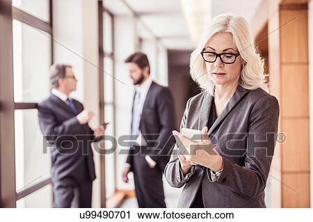Stock Image - Businesswoman reading smartphone update in office corridor. Fotosearch
