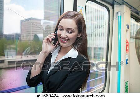 Picture - Businesswoman using cellphone in Docklands Light Railway train, London. Fotosearch