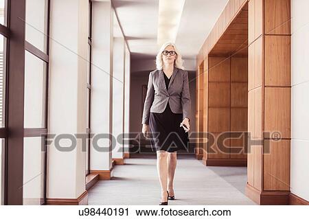 Businesswoman walking along office corridor View Large Photo Image Stock Image - Businesswoman walking along office corridor. Fotosearch