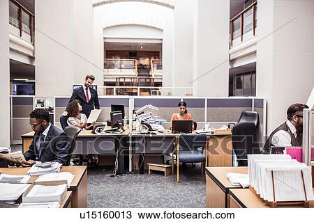 Stock Image - Businesswomen and businessmen busy working in office. Fotosearch