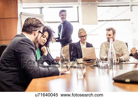 Stock Photography - Businesswomen and men discussing ideas at conference table presentation. Fotosearch