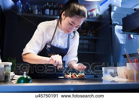 Stock Image - Chef in commercial kitchen seasoning food. Fotosearch