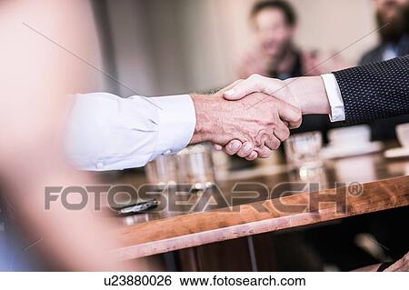 Stock Photograph - Close up of businesswoman and man shaking hands in board team meeting. Fotosearch