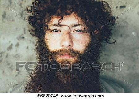 Stock Photography - Close up portrait of young male hipster with brown curly hair and beard. Fotosearch
