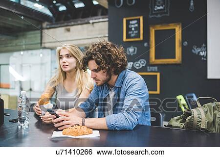 Stock Photograph - Co-workers having morning break at table. Fotosearch