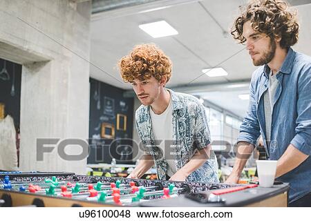 Stock Photo - Co-workers playing foosball at break. Fotosearch
