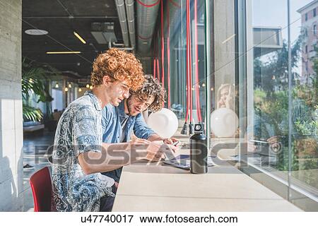 Stock Photo - Co-workers working on laptop beside bar counter by window. Fotosearch