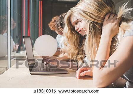 Stock Photography - Co-workers working on laptop beside bar counter by window. Fotosearch