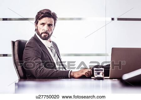 Confident businessman looking over shoulder from office desk View Large Photo Image Stock Image - Confident businessman looking over shoulder from office desk. Fotosearch