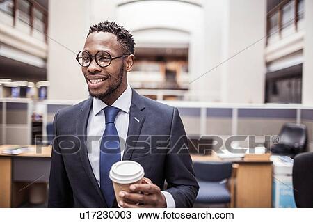 Stock Image - Confident young businessman with takeaway coffee in office. Fotosearch