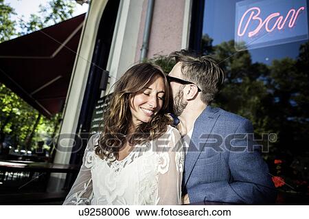 Stock Photograph - Couple head to head smiling outside of bar, using smartphone, Berlin, Germany. Fotosearch