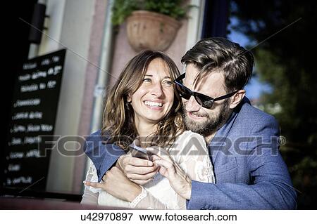 Couple hugging and smiling, using smartphone, Berlin, Germany View Large Photo Image Stock Photo - Couple hugging and smiling, using smartphone, Berlin, Germany. Fotosearch