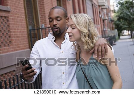 Stock Image - Couple looking at mobile phone during walk. Fotosearch