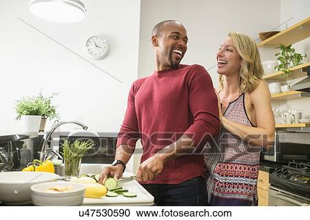 Stock Image - Couple preparing dinner in kitchen and laughing. Fotosearch