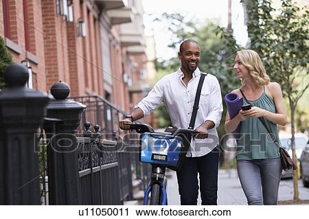 Stock Image - Couple walking with bicycle and exercising mat. Fotosearch