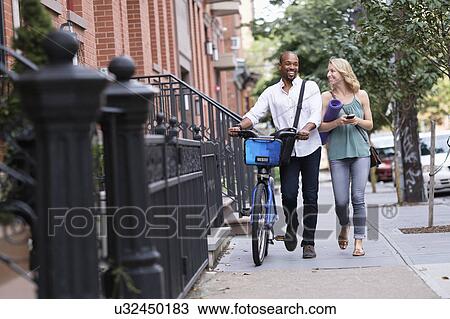 Stock Image - Couple walking with bicycle and exercising mat. Fotosearch