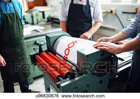 Stock Photograph - Craftspeople being shown how to use letterpress machine in book arts workshop, mid section. Fotosearch