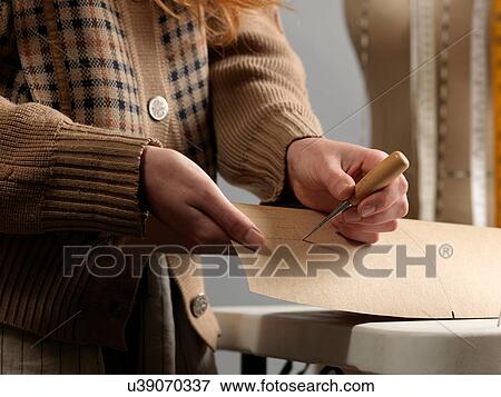 Stock Photo - Cropped close up of young female fashion designer piercing dressmaker's pattern. Fotosearch