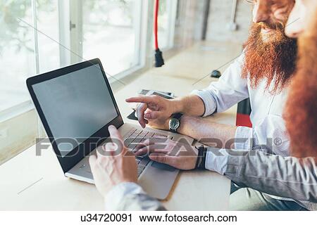 Stock Image - Cropped shot of male twins working on laptop in office. Fotosearch