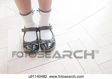 Stock Image - Cropped shot of schoolgirl wearing shoes and ankle socks standing on parquet floor. Fotosearch
