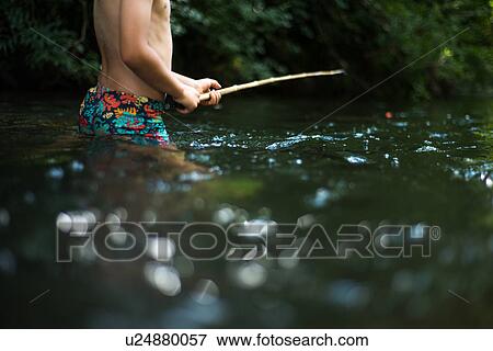 Stock Photo - Cropped view of boy waist deep in water holding stick. Fotosearch