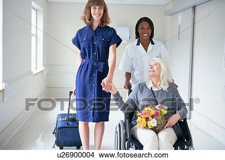 Picture - Daughter and hospital orderly pushing senior female patient in wheelchair. Fotosearch