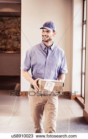 Stock Image - Delivery man carrying package in office. Fotosearch