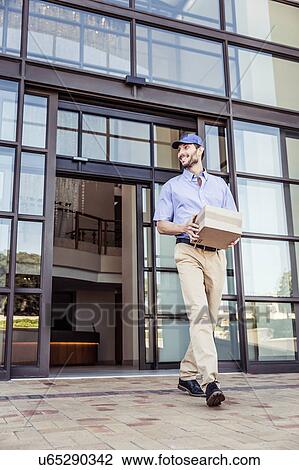 Delivery man carrying package outside office View Large Photo Image Stock Image - Delivery man carrying package outside office. Fotosearch