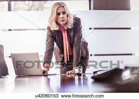 Stock Image - Determined businesswoman leaning forward on boardroom table. Fotosearch