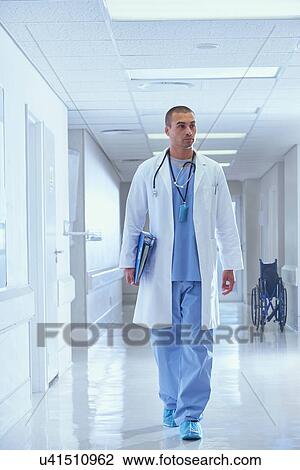 Doctor walking along hospital corridor carrying medical notes View Large Photo Image Stock Image - Doctor walking along hospital corridor carrying medical notes. Fotosearch