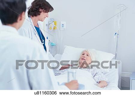 Stock Photograph - Doctors explaining to senior female patient in hospital bed. Fotosearch