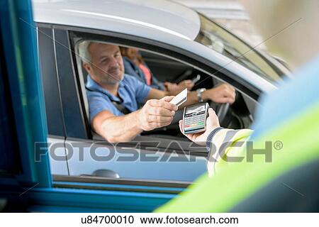 Stock Image - Driver in car paying toll booth at bridge using contactless card payment technology. Fotosearch