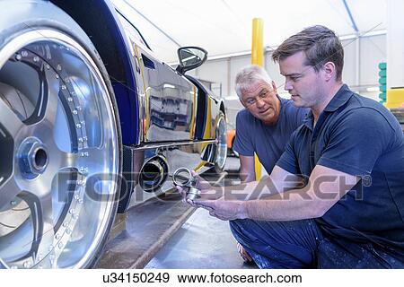 Stock Photo - Engineer and apprentice discussing exhaust valve on sports car in research and development facility of factory. Fotosearch