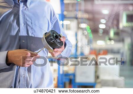 Stock Image - Engineer holding 3D printed exhaust valve actuator in factory. Fotosearch