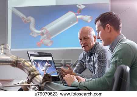 Stock Image - Engineers discussing CAD drawings onscreen of exhaust system in factory. Fotosearch