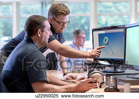 Stock Photography - Engineers discussing CAD drawings onscreen of exhaust valve actuator in factory. Fotosearch