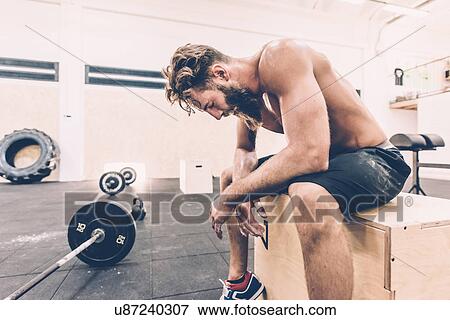 Exhausted male cross trainer taking a break from weightlifting in gym View Large Photo Image Stock Photo - Exhausted male cross trainer taking a break from weightlifting in gym. Fotosearch