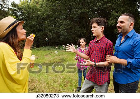 Family fooling around outdoors, mother blowing bubbles at family View Large Photo Image Stock Image - Family fooling around outdoors, mother blowing bubbles at family. Fotosearch