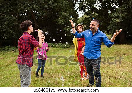 Family fooling around outdoors, teenage boy blowing bubbles at family View Large Photo Image Stock Photography - Family fooling around outdoors, teenage boy blowing bubbles at family. Fotosearch