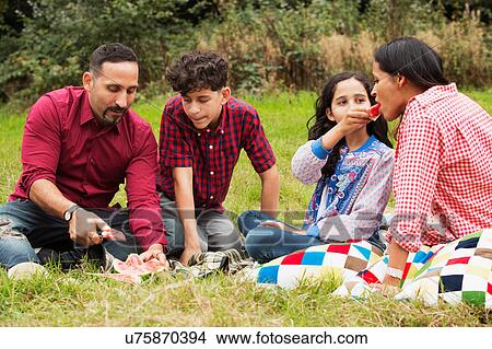 Family sitting outdoors, on picnic blanket, eating watermelon View Large Photo Image Picture - Family sitting outdoors, on picnic blanket, eating watermelon. Fotosearch