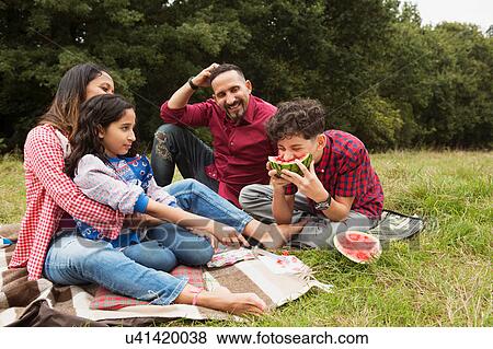Family sitting outdoors, on picnic blanket, son eating watermelon View Large Photo Image Stock Photo - Family sitting outdoors, on picnic blanket, son eating watermelon. Fotosearch