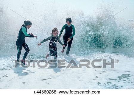 Stock Photo - Family wearing wet suits running from waves. Fotosearch