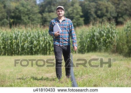 Stock Image - Farmer in field carrying paperwork. Fotosearch